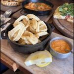 A table full of food, including a bowl of garlic bread, a bowl of pasta, and a bowl of sausage.