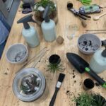 A table full of gardening tools and supplies, including a spray bottle, a pair of scissors, and a wine glass.