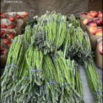 A table full of green asparagus, with some apples and tomatoes nearby.