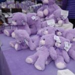 A table full of purple teddy bears for sale.