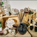 A table full of various vases and bowls, some with flowers in them, and a few with dried flowers.