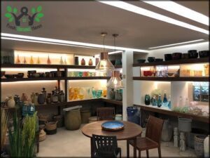 A table with a blue plate on it sits in front of a shelf filled with various vases and bowls.