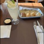 A table with a glass of lemonade, a basket of bread, and a fork and knife.