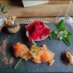A table with a variety of food items, including a salmon dish, a bowl of fruit, and a wine glass.