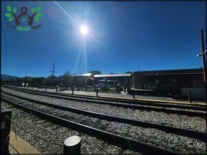 A train station with a train on the tracks and a sunny day.