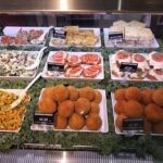 A variety of foods are displayed in a buffet line, including pasta, bread, and vegetables.