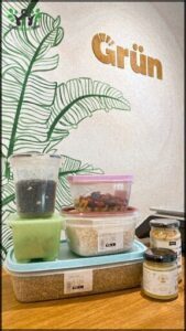 A variety of foods are displayed on a table, including a bowl of rice, a jar of beans, and a container of fruit.