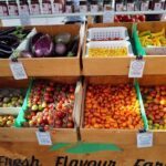 A variety of fresh fruits and vegetables are displayed in wooden crates, including tomatoes, peppers, and squash.
