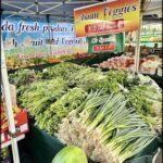 A variety of fresh vegetables are displayed at a market, including broccoli, asparagus, and other produce.