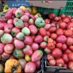 A variety of fruits and vegetables are displayed in boxes, including tomatoes, apples, and peaches.