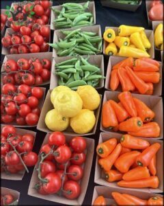 A variety of fruits and vegetables are displayed in boxes, including tomatoes, lemons, and peppers.
