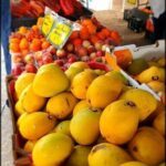 A variety of fruits are displayed at a market, including oranges, apples, and mangos.