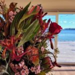A vase filled with flowers sits on a table, overlooking a beautiful ocean view.