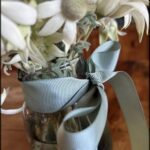 A vase filled with white flowers and a blue bow.