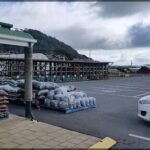 A white car is parked in front of a building with a large pile of bags and ropes.