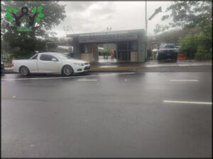 A white car is parked in front of a greyhound racing facility.