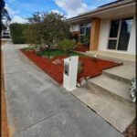 A white mailbox sits on a red mulch bed in front of a house.