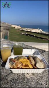 A white paper plate with a variety of food items sits on a ledge overlooking the ocean.