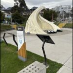 A white sculpture of a violin is displayed in a park.