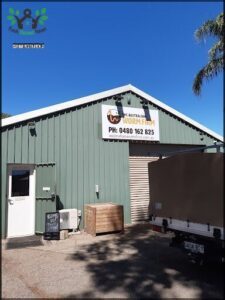 A white truck is parked in front of a green building with a sign that reads "The Australian Farm."