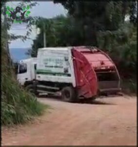A white truck with a red garbage can on the back is parked on a dirt road.