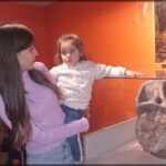 A woman and a young girl are standing in front of a display, with the woman holding the little girl.