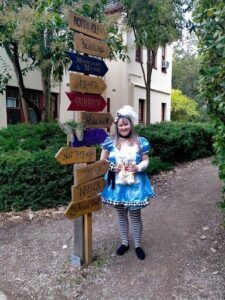 A woman dressed in a blue and white costume stands in front of a sign that reads "This way to Neverland."