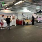 A woman in a black shirt and a man in a white shirt are standing in front of a food stand.