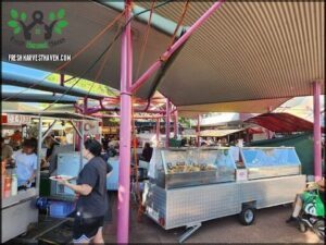 A woman in a black shirt is holding a plate of food, likely enjoying a meal at a food stand.
