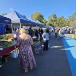 A woman in a floral dress is walking past a market stand, possibly looking for fresh produce.