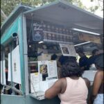 A woman in a pink tank top is ordering food from a food truck.