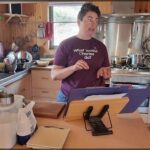 A woman in a purple shirt is standing in a kitchen, holding a piece of paper.