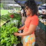 A woman in an orange shirt is holding lettuce at a market.