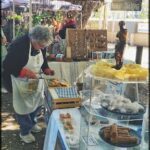 A woman is cutting a cake at a market stand.