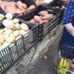 A woman is shopping for potatoes and bananas at a market.