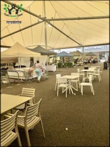 A woman is shopping in a marketplace with white tables and chairs.