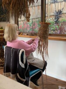 A woman is sitting in a chair, working on a craft project.