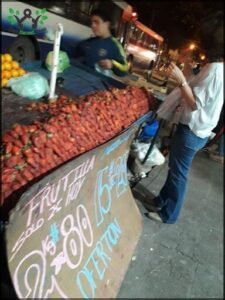 A woman is standing in front of a fruit stand, looking at the strawberries.