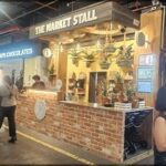 A woman is walking past a storefront with a brick wall and a sign that says "The Market Stall."