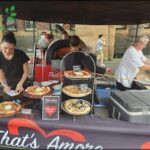 A woman is writing on a piece of paper in front of a table full of pizzas.