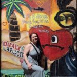 A woman poses in front of a mural with a heart on it.