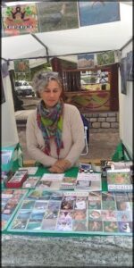 A woman sits at a table with a variety of items, including CDs and books.
