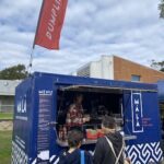 A woman stands behind a food truck, serving customers.