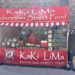 A woman stands behind a red and white food stand, selling street food.