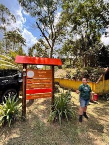 A woman stands in front of a sign that reads "Planta de feliz" in a park.