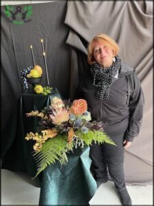 A woman stands in front of a table with a vase of flowers on it.