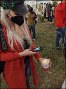 A woman wearing a mask and a red sweater is looking at her cell phone.