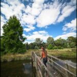 A woman wearing a red hat and black pants is standing on a bridge over a river.