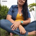 A woman wearing a yellow shirt and blue jeans is sitting in the grass.