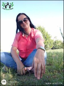 A woman wearing sunglasses and a pink shirt is sitting on the grass.